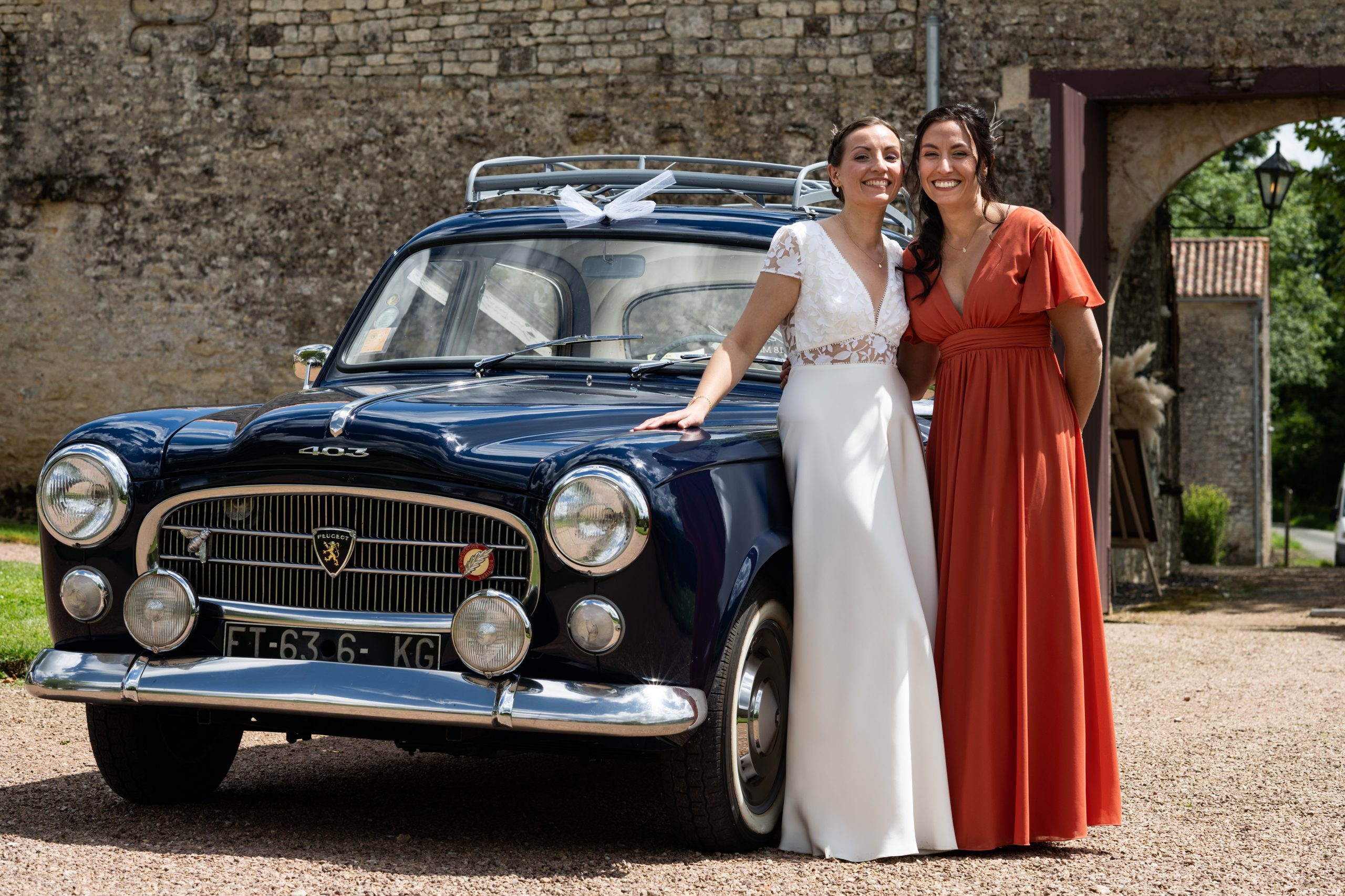 Ameline Blot et sa sœur posant devant une voiture de collection lors d'un mariage, exemple de photographie de mariage pour professionnels.