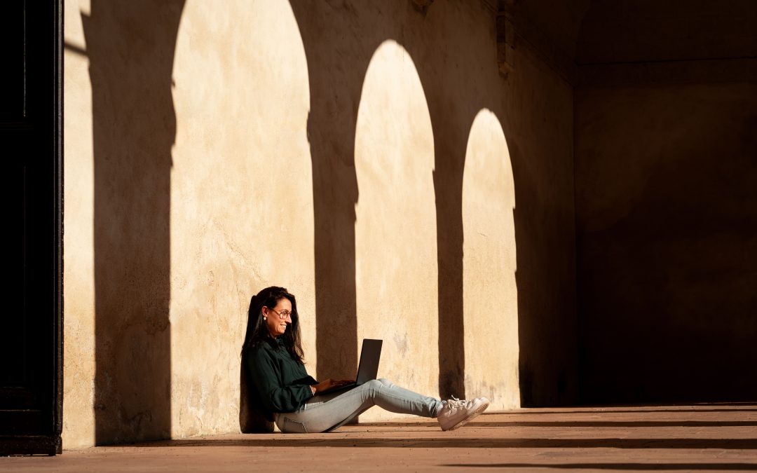 Ameline Blot, accompagnatrice pour photographes, travaillant sur son ordinateur portable en extérieur sous des arches ensoleillées.
